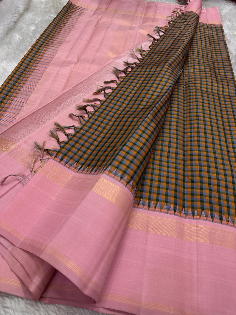 Nirai – A Madras-Inspired Kanchipuram Silk in Amber & Pastel Pink.
Woven with fine podi kattam checks in black, amber orange, and grey.
The pastel pink border with pillayar moggu detailing adds softness, with a  seer zari pallu