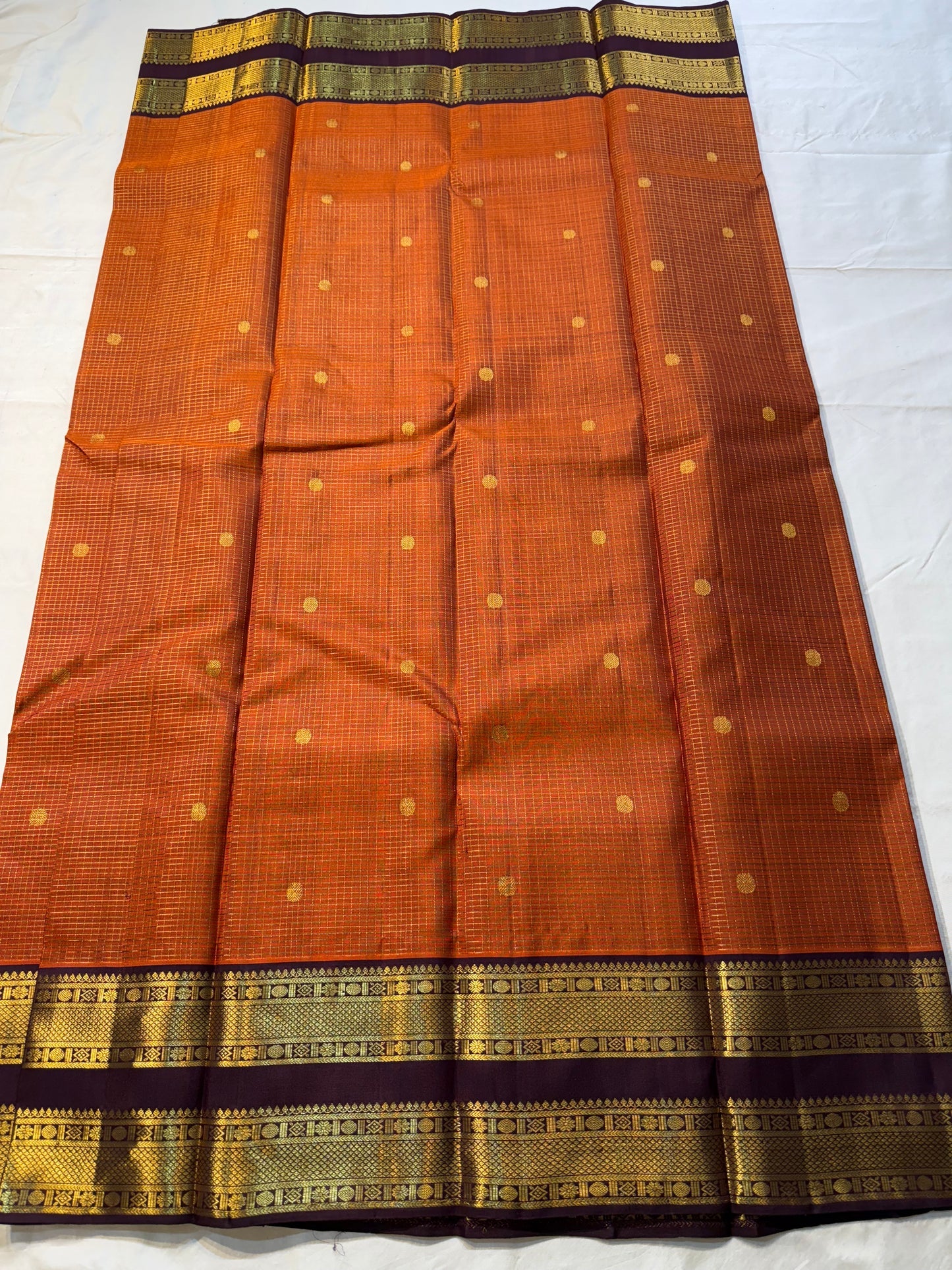 Rust Orange Kattam Rettapet – Pure Silk Kanchipuram Saree
Rust Orange Body with Petite Gold Buttas & Fine Kattam Grid
Deep Aubergine Rettapet Korvai Double-Line Contrast Border
Rich Zari Diamond & Chevron Brocade Pallu
Comes with Contrast Aubergine Blouse