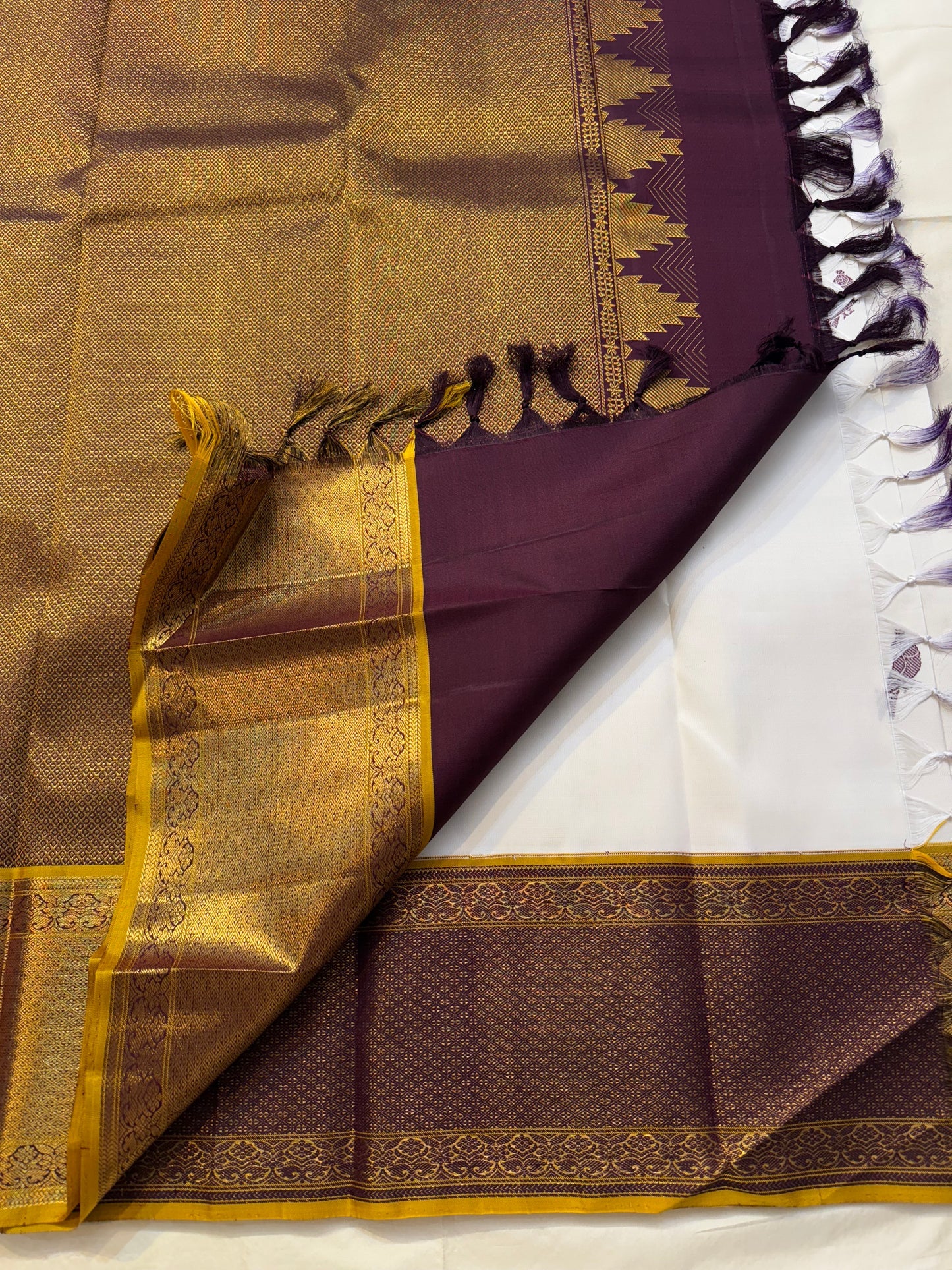 Pallu view of Kanchipuram silk saree in deep plum with dense antique-gold zari weaving and temple-inspired border