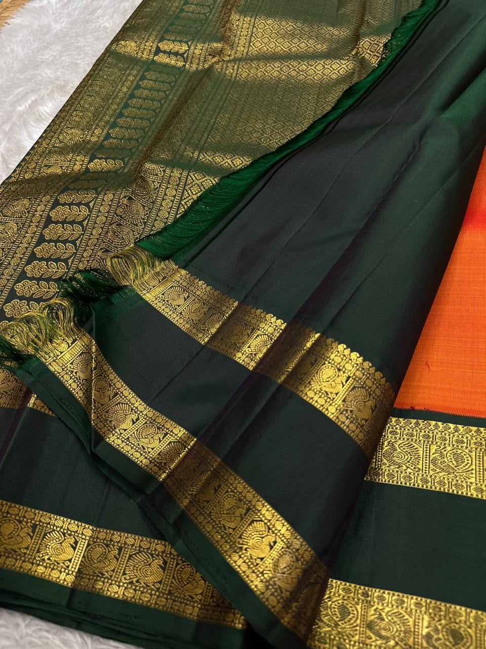Riya – Orange Silk Saree with Dark Green Zari Border
Radiating warmth and festive charm, Riya  glows in a rich ombré of orange and vermilion, adorned with dainty gold butta motifs that shimmer gently with movement.