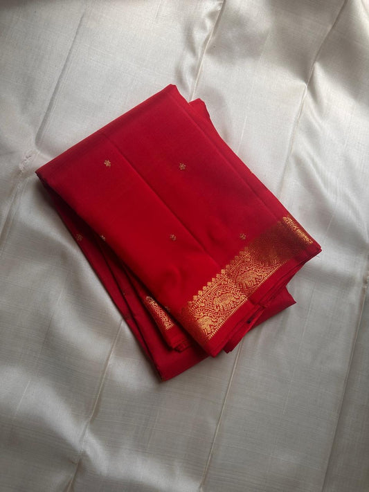 Mahima –red
A luminous red pure silk Kanchipuram drape adorned with delicate baby  kamalam buttas. The petite border features muthu seer and zari-woven elephants with floral vines. Its grand pallu showcases annams, golden grids, and Rudhraksham seer.