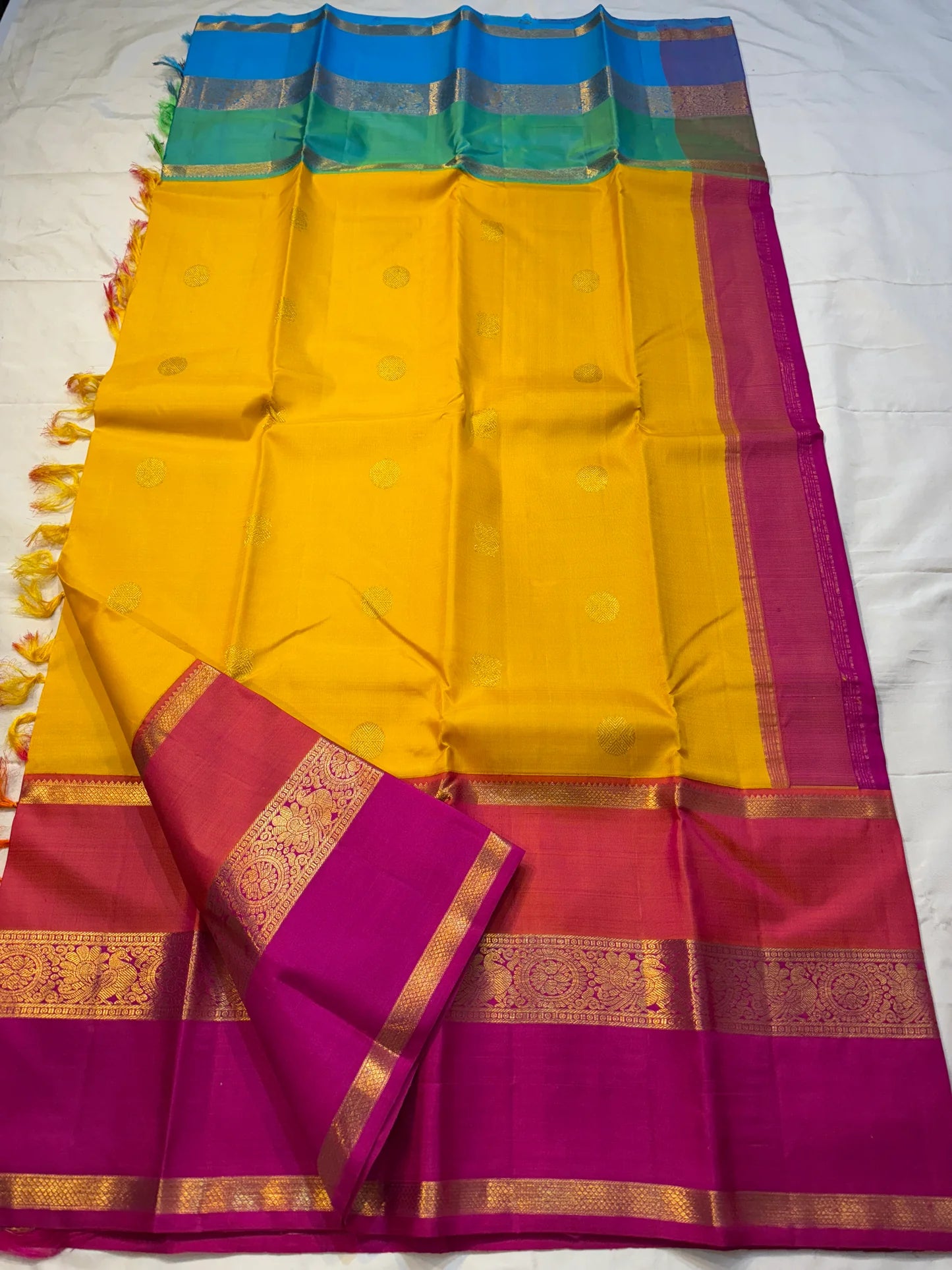 Varna Jaalam — Kanchipuram Pure Silk

Manjal yellow body with gold chakram buttas

Rani pink korvai border with floral & coin zari panels

Magenta–orange chevron pallu with blue–green color block top

Silk Mark Certified • Free Shipping within USA •
