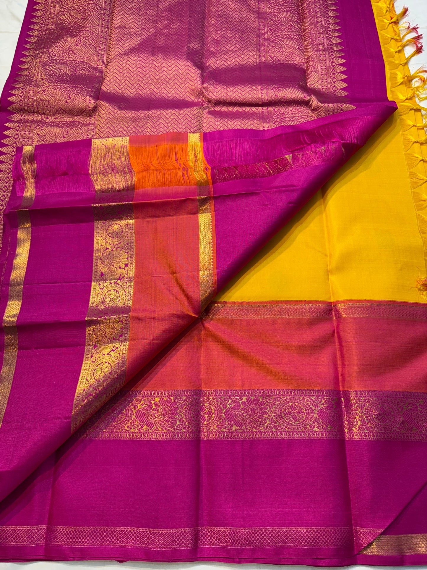 Varna Jaalam — Kanchipuram Pure Silk

Manjal yellow body with gold chakram buttas

Rani pink korvai border with floral & coin zari panels

Magenta–orange chevron pallu with blue–green color block top

Silk Mark Certified • Free Shipping within USA •