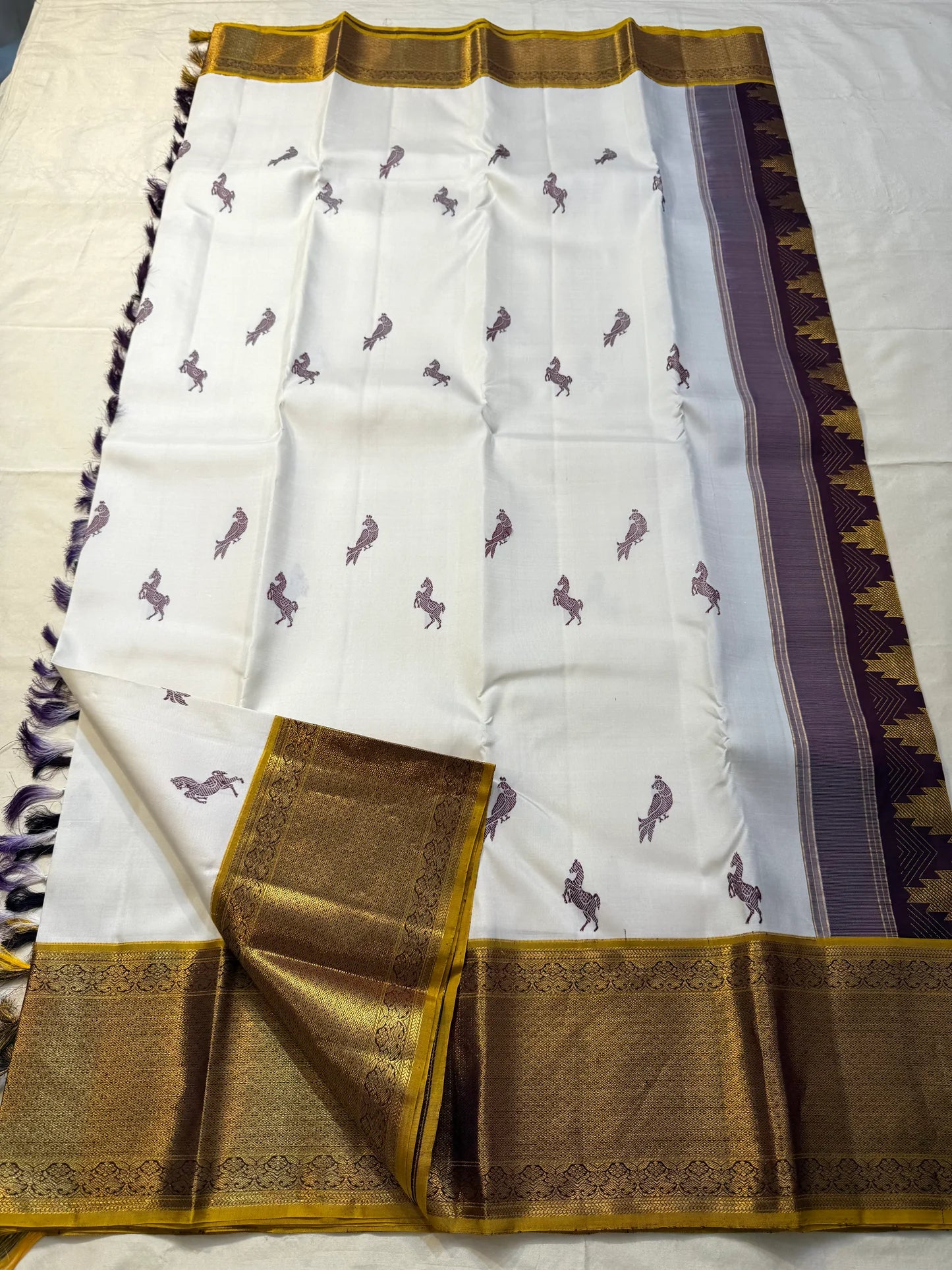 Open body view of ivory Kanchipuram silk saree featuring scattered horse and parrot motifs with gold zari borders on both sides