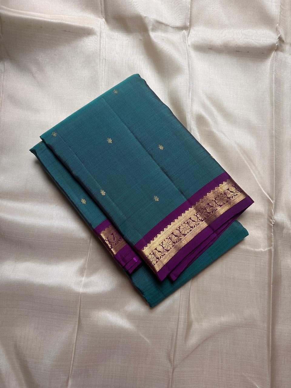 Folded teal pure Kanchipuram silk saree with purple zari woven border, shipped from New Jersey USA.