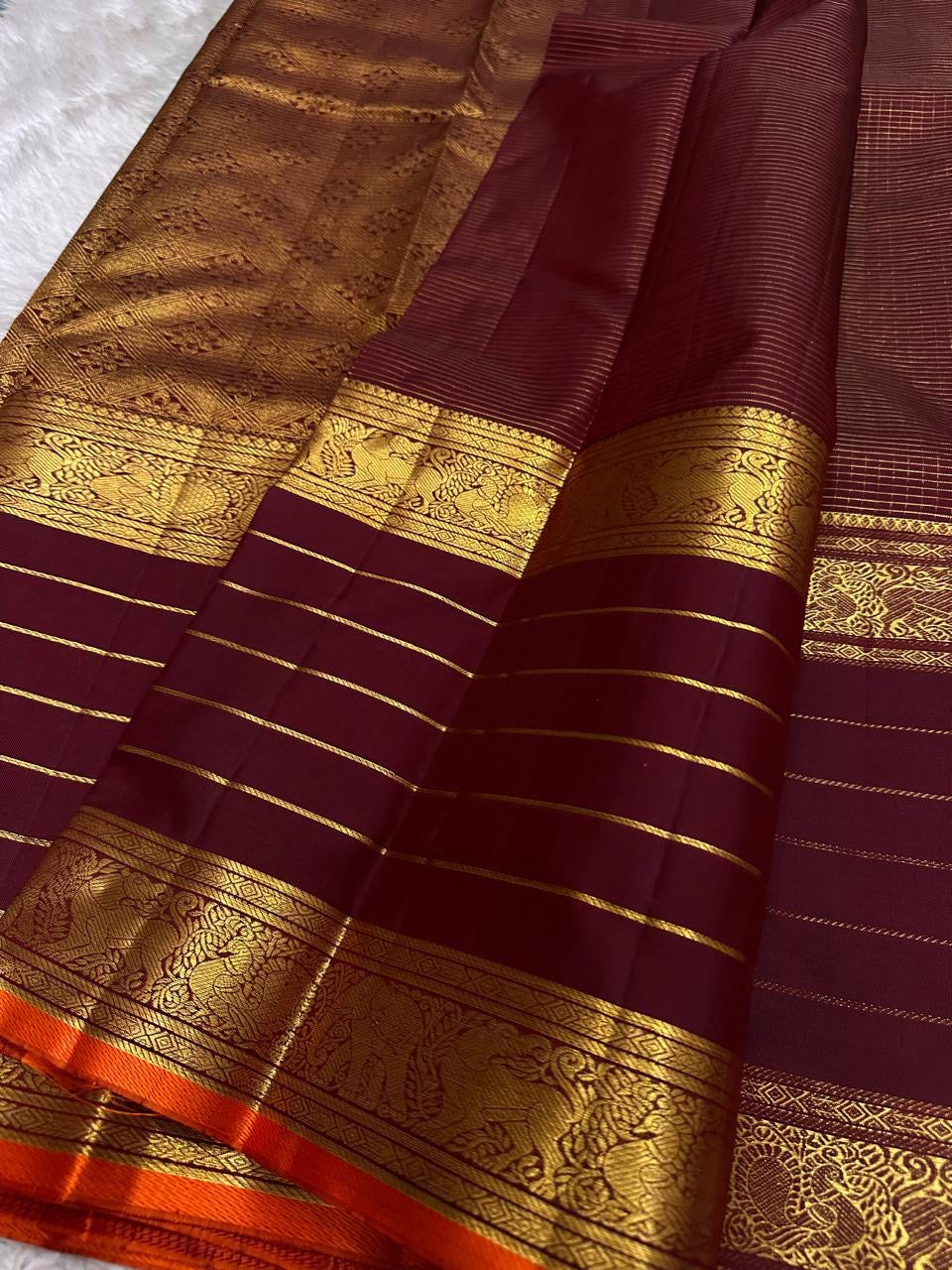 Close-up of maroon Kanchipuram silk saree pallu featuring dense gold zari weaving and traditional motif panels.