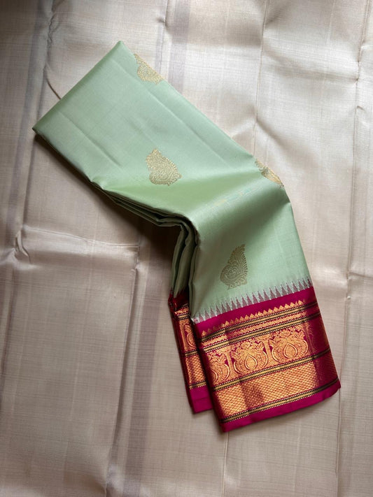 Mohana 🌿✨ – Graceful Cardamom Pistachio Green Pure Kanchipuram Silk Saree with Handwoven Zari Peacocks 🦚, Deep Purple Peacock Border 💜🦚, Pillayar Moggu Detailing 🌺, & Intricately Woven Grid Zari Pallu 🎀💛