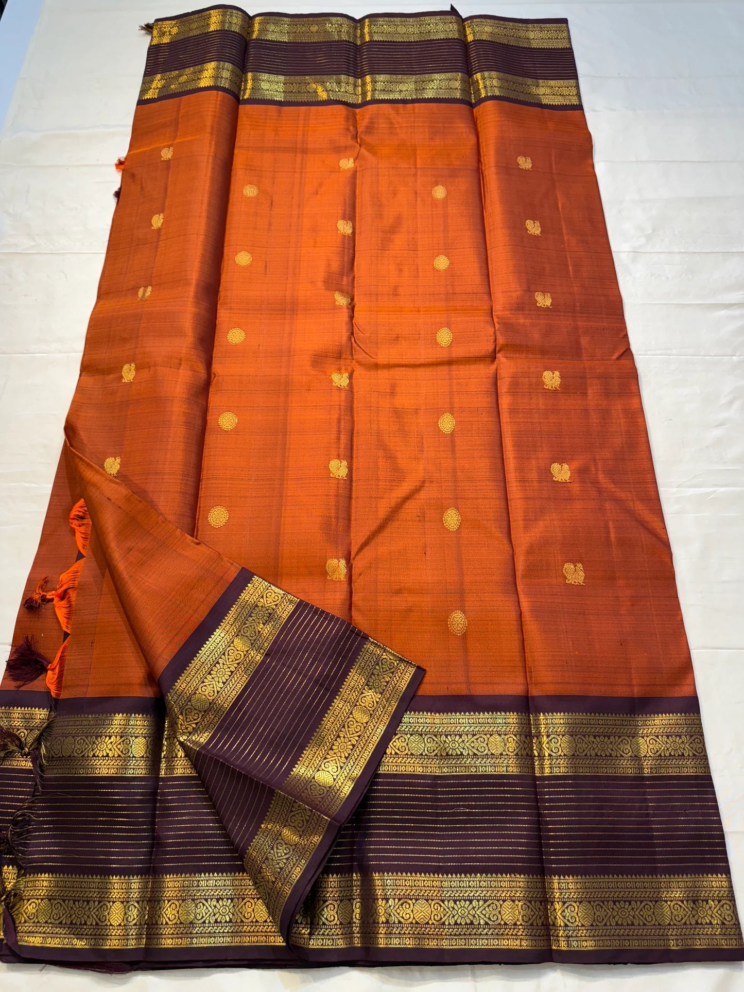 🧡 

Swarnamala — Korvai Kanchipuram Pure Silk

Rust-orange body with radiant gold chakram buttas

Deep purple korvai borders with rich zari detailing

Striped zari brocade pallu with temple-inspired motifs

Silk Mark Certified • Free Shipping within USA