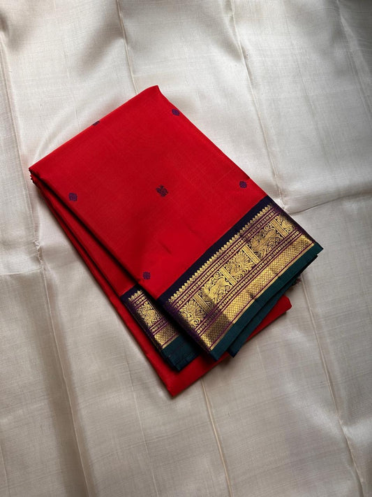 A stunning blend of red and royal blue with a green edge, featuring Kamalam Chakram motifs and a majestic Vanasingaram border, paired with a Kili-themed Kanchipuram pallu.