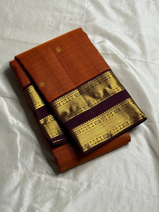 Rust Orange Kattam Rettapet – Pure Silk Kanchipuram Saree
Rust Orange Body with Petite Gold Buttas & Fine Kattam Grid
Deep Aubergine Rettapet Korvai Double-Line Contrast Border
Rich Zari Diamond & Chevron Brocade Pallu
Comes with Contrast Aubergine Blouse