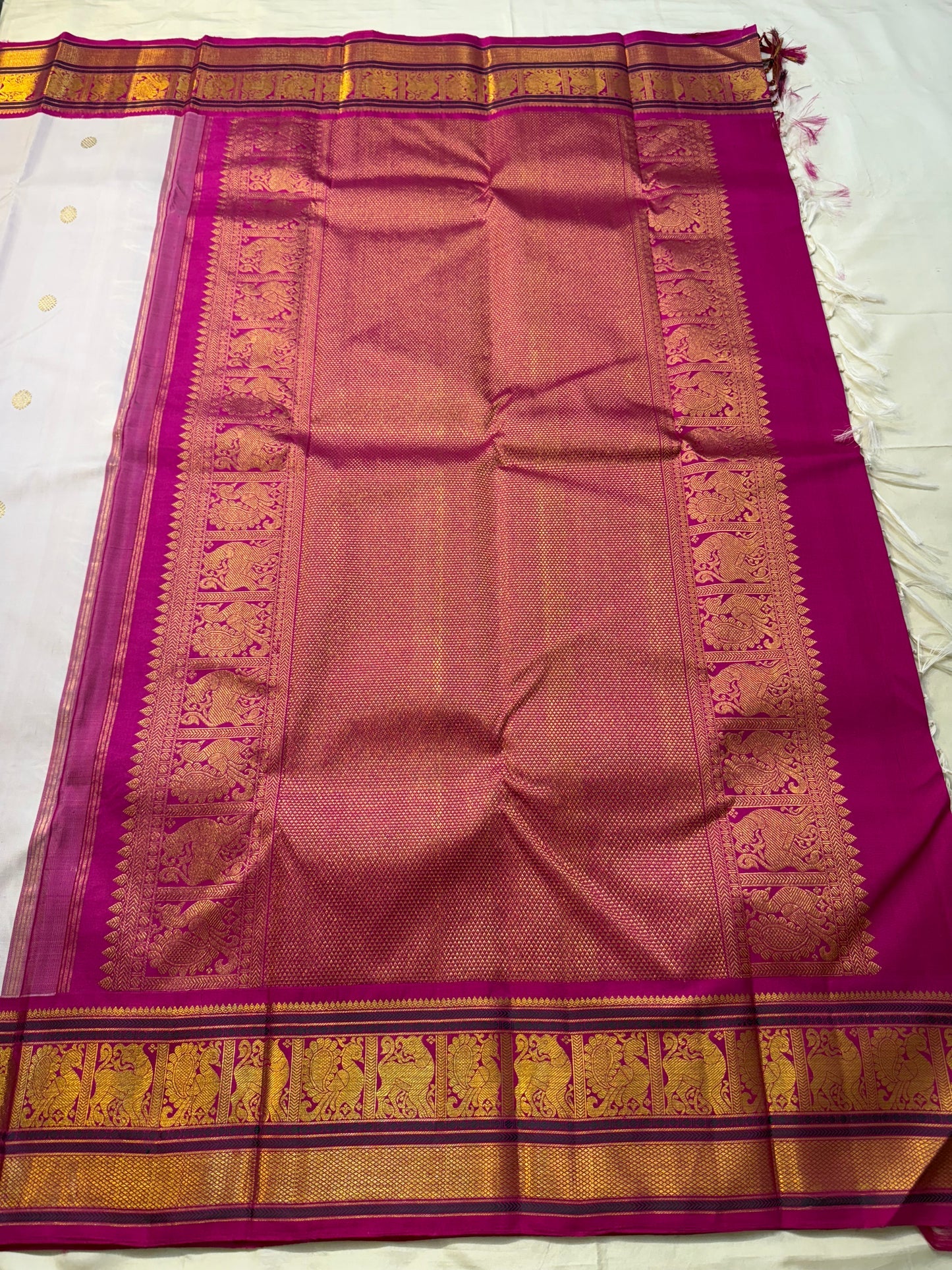 Fuchsia pallu spread out with dense gold zari weave and framed motif panels, with tassels visible at one end.