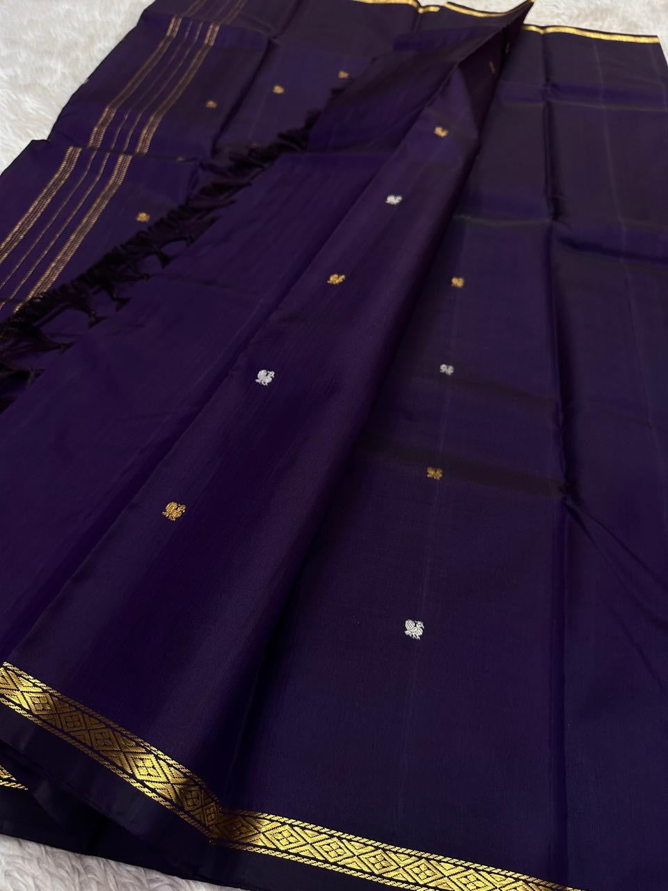Full layout of purple Kanchipuram silk saree with evenly spaced gold buttas and simple zari pallu and border.