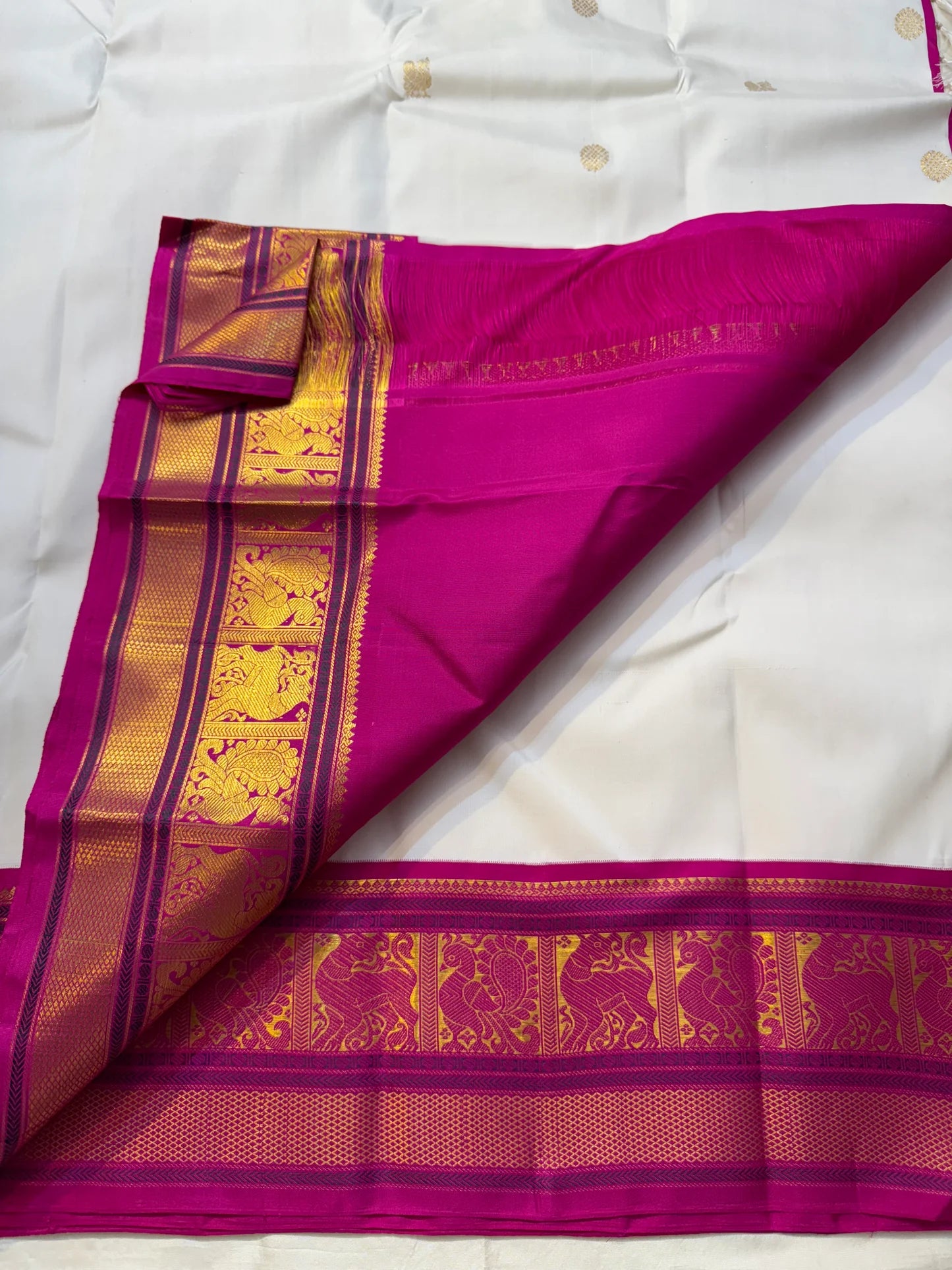 Close-up of fuchsia pallu with gold zari woven motifs and border, partially folded over the ivory saree body.