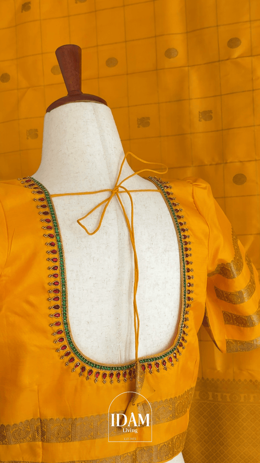 Yellow blouse with intricate embroidery on a mannequin against a yellow checkered background