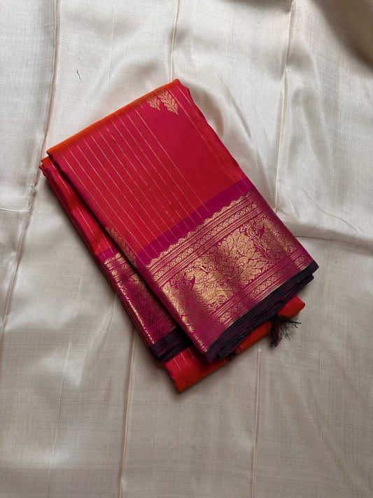 Sharvani – Orange & Magenta Pure Silk Kanchipuram Saree
Featuring zari-woven stripes across the body for subtle structure.
Bold magenta border with rice reed and peacock motifs, finished with a green selvedge.
