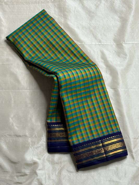 Mayil Pachai Kattam
Pure Kanchipuram Silk Saree – Peacock Green & Mustard Micro Checks
Royal blue korvai borders with gold floral zari detailing
Grand zari pallu with traditional zari weaving
Ships in two weeks free shipping, silk mark certified