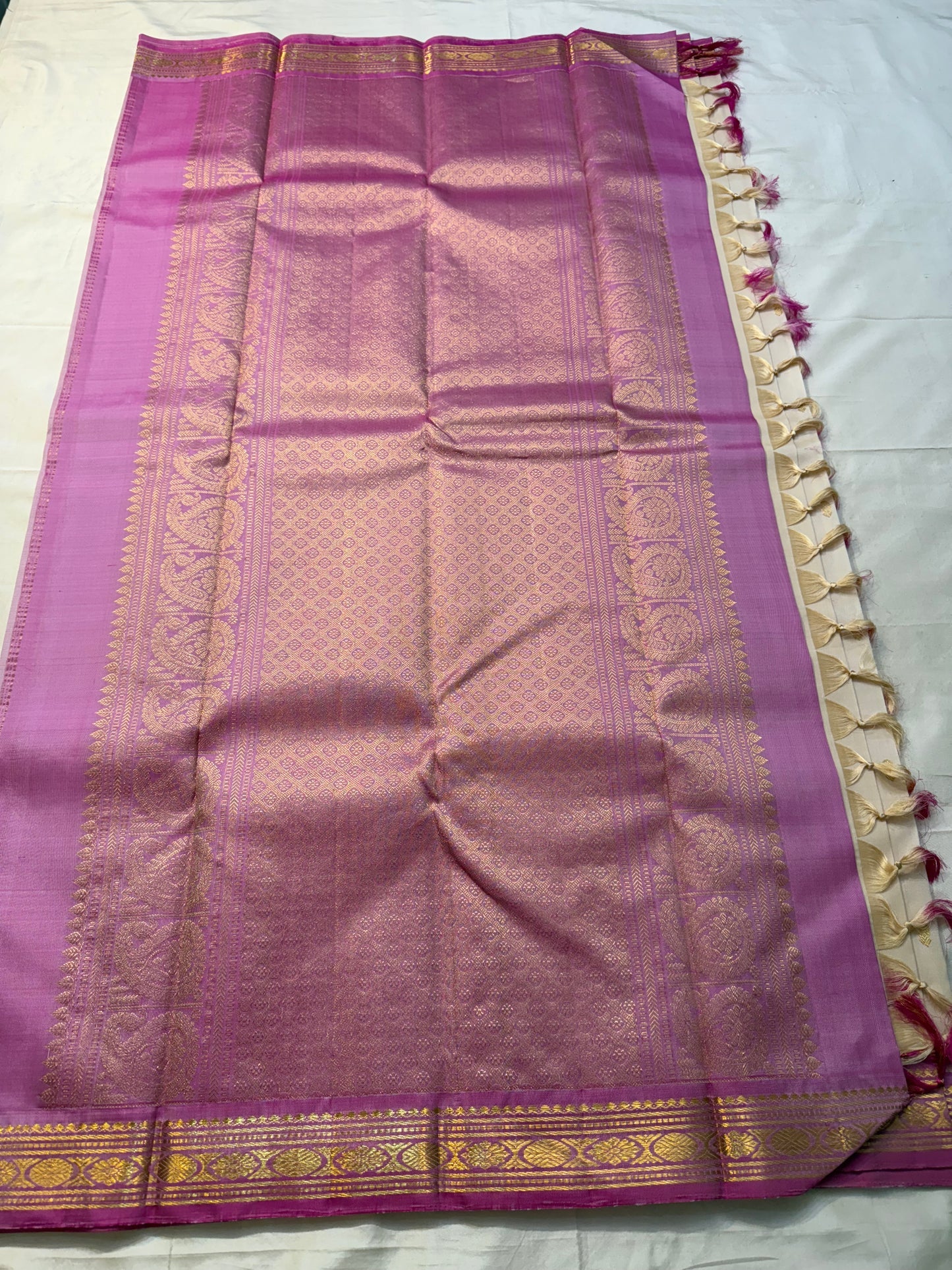 Magenta-lavender pallu laid out with allover gold zari woven design and cream tassels along the edge on a white sheet.
