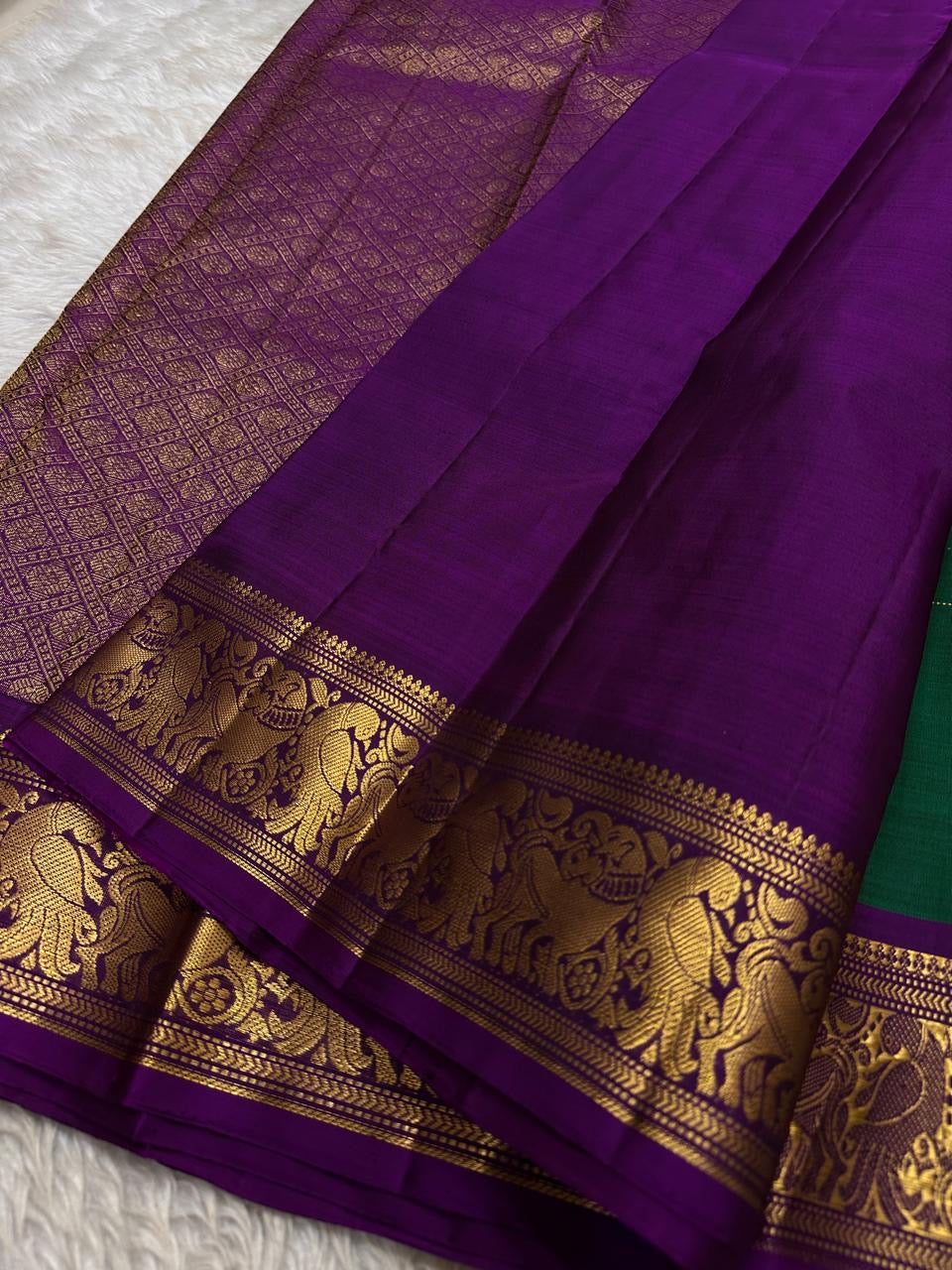 Sorgavaasal Kili – Pure Silk Kanchipuram Saree in Teal with Purple Zari Kattam
Intricately handwoven with traditional zari kattam checks and adorned with exquisite zari-woven Yazhi buttas, this saree features a vibrant teal body paired with a regal purple