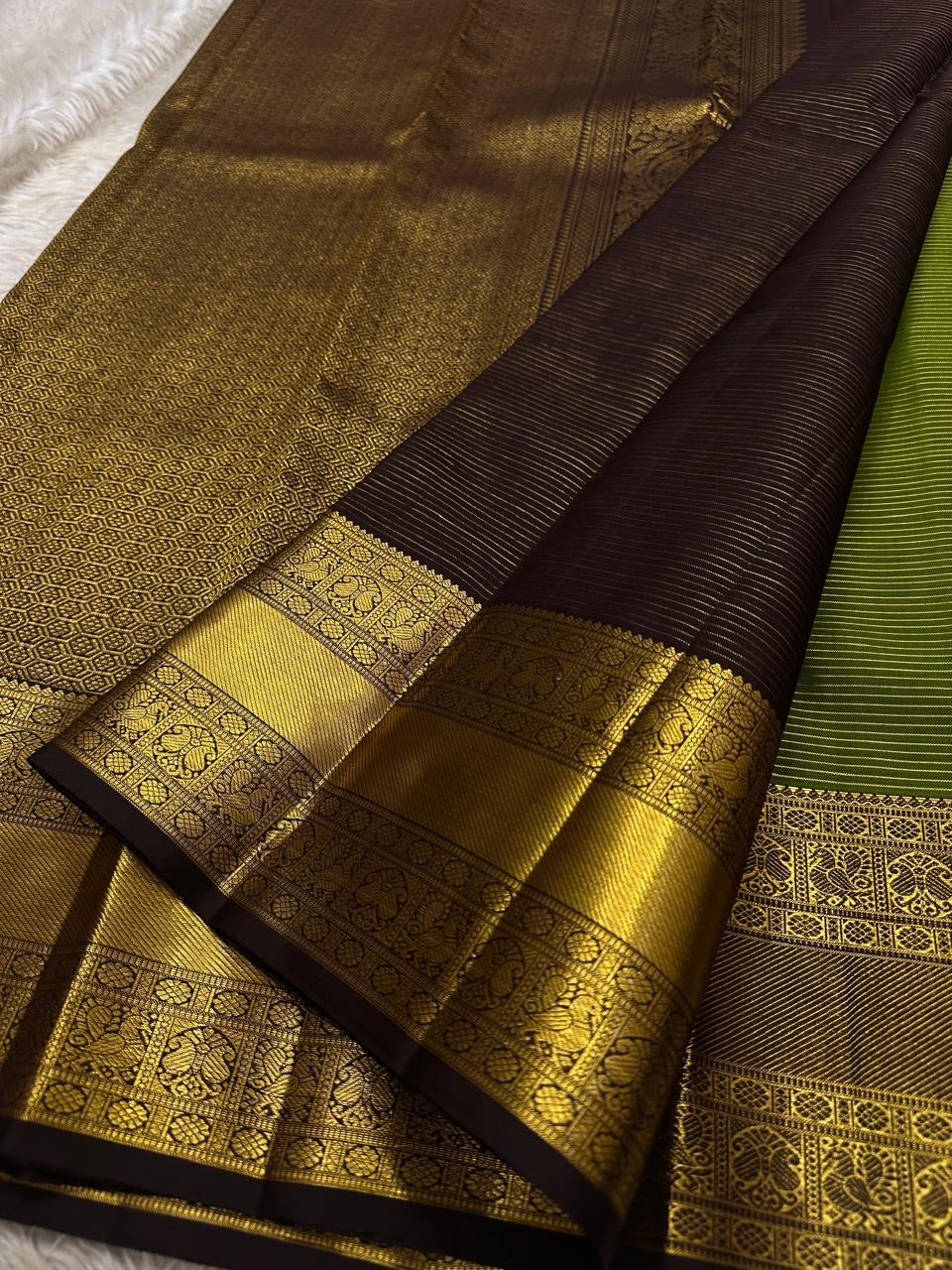 Forest Gold – Pure Kanchipuram Silk Saree
Leaf-green body with fine pin stripes.
Zari leaf buttas for subtle sparkle.
Coffee-maroon korvai border in antique gold.

Silk Mark Certified, delivery in 2 weeks