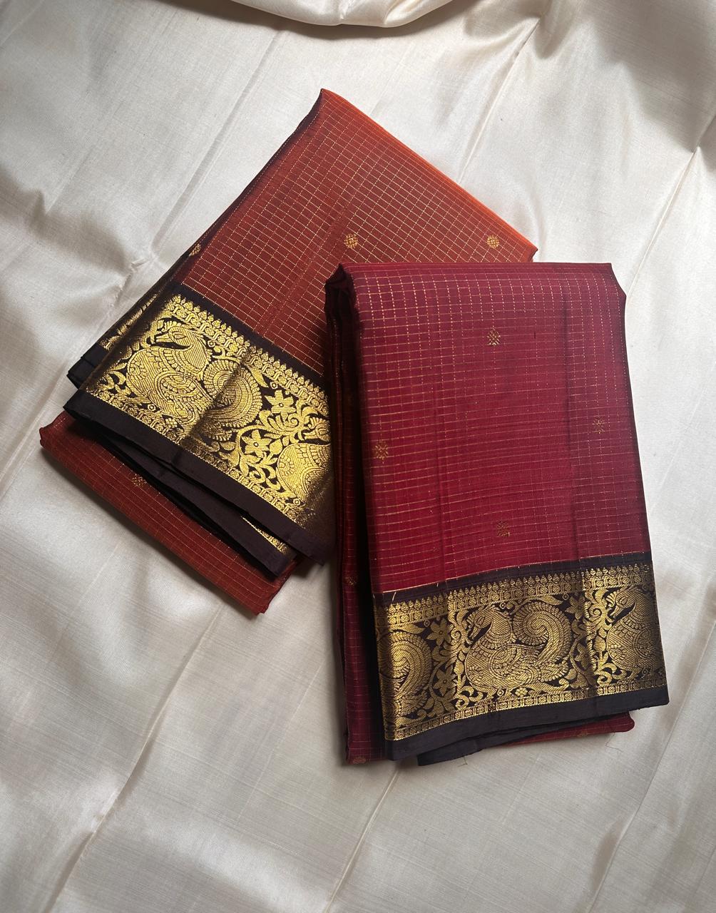 Mantra – Ruby Red coffee brown Kanchipuram Silk Saree with zari Checks with small buttas all over and Antique Peacock zari Border  showcasing regal peacocks and floral vines. A richly detailed pallu completes this heritage Zari kattam