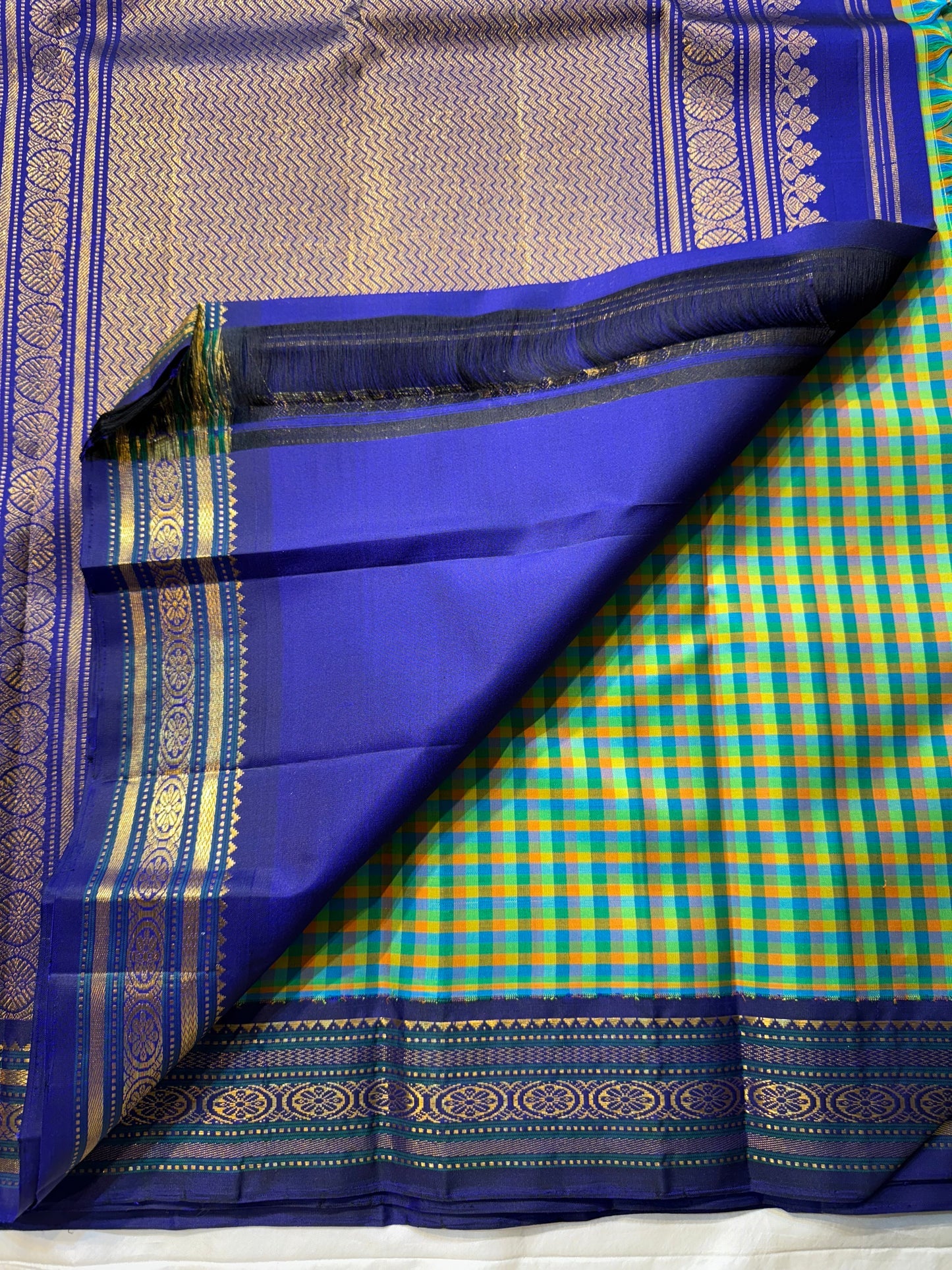 Mayil Pachai Kattam
Pure Kanchipuram Silk Saree – Peacock Green & Mustard Micro Checks
Royal blue korvai borders with gold floral zari detailing
Grand zari pallu with traditional zari weaving
Ships in two weeks free shipping, silk mark certified