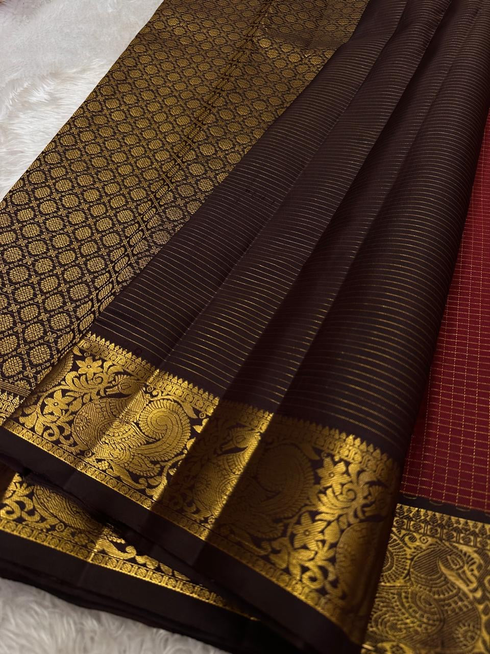 Mantra – Ruby Red coffee brown Kanchipuram Silk Saree with zari Checks with small buttas all over and Antique Peacock zari Border  showcasing regal peacocks and floral vines. A richly detailed pallu completes this heritage Zari kattam