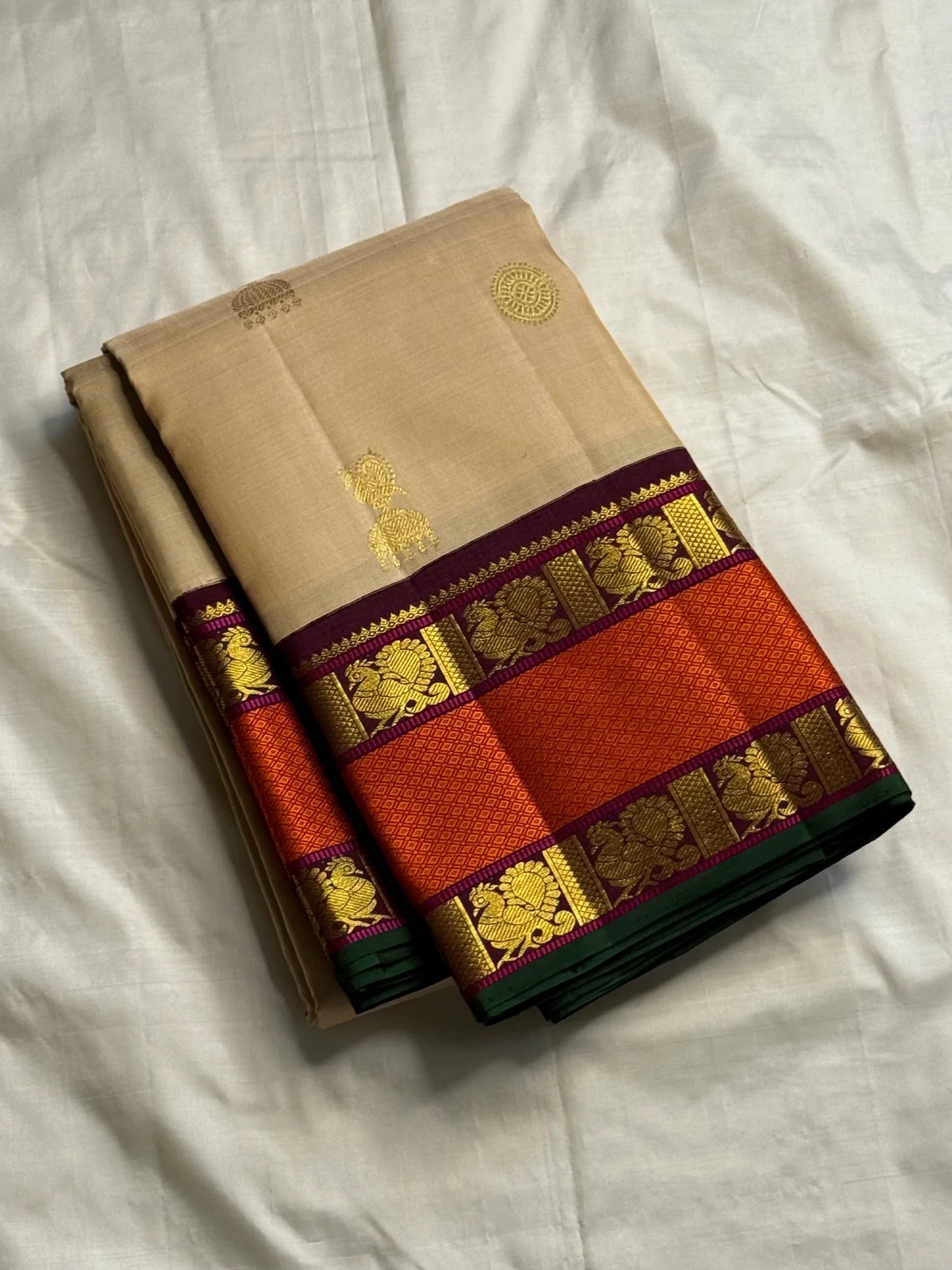 Pure Kanchipuram silk saree folded in biscuit beige with small gold buttas and rust orange zari woven border, maroon striping, and green edge
