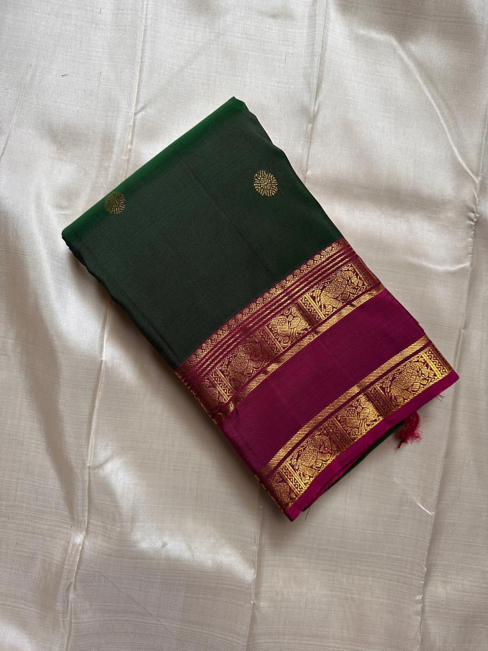 Emerald green silk saree fold with gold zari buttas and magenta border with woven zari panels