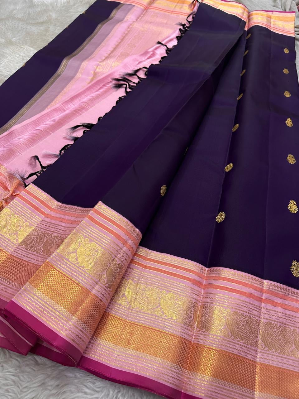Shyamala—named after the deep, dark shade it embodies 💜 A pure Kanchipuram silk masterpiece with a rich purple body sprinkled with golden zari buttas. The contrast pink border glows with floral and paisley zari motifs, accented in coral and rose-gold, wh