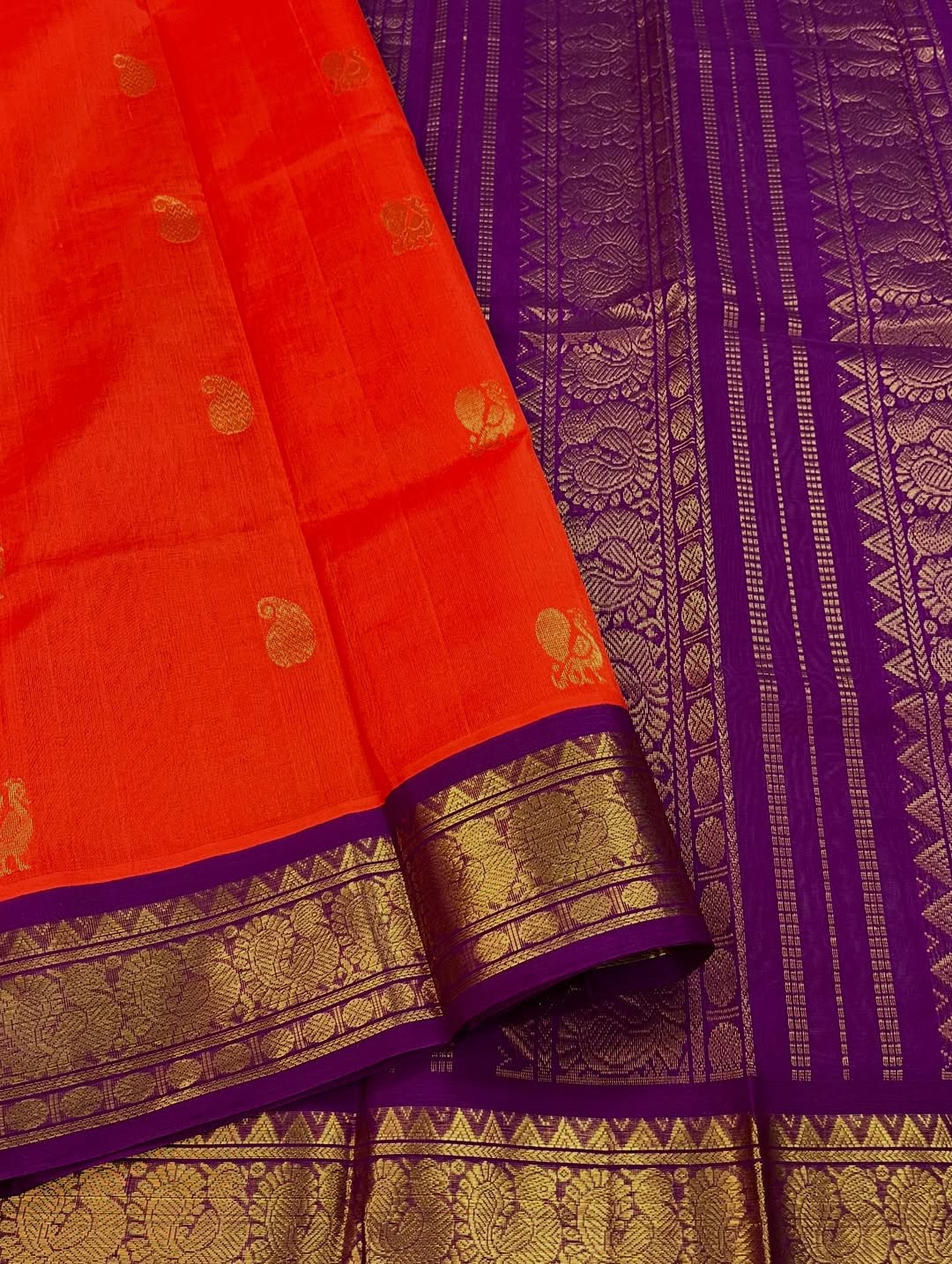 An exquisite blend of tradition and vibrancy, this silk cotton saree features a radiant orange body adorned with elegant gold zari buttas, The rich contrast border and pallu in royal purple and intricately woven with traditional gold zari motif