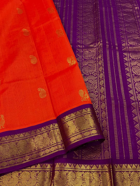 An exquisite blend of tradition and vibrancy, this silk cotton saree features a radiant orange body adorned with elegant gold zari buttas, The rich contrast border and pallu in royal purple and intricately woven with traditional gold zari motif