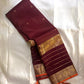 Partly opened maroon Kanchipuram silk saree showing fine grid checks on the body and gold zari striped border with yali and elephant motifs.