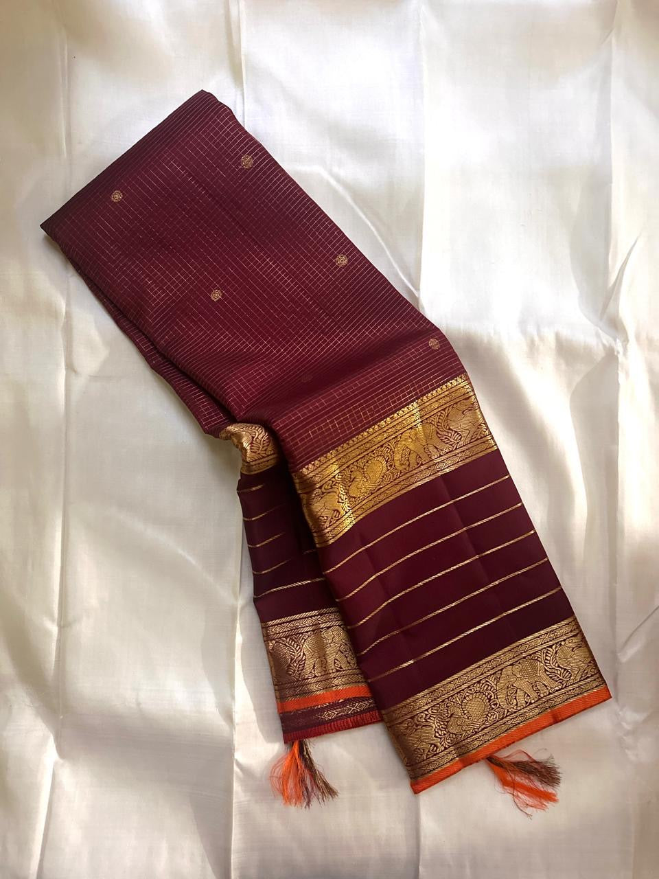 Partly opened maroon Kanchipuram silk saree showing fine grid checks on the body and gold zari striped border with yali and elephant motifs.