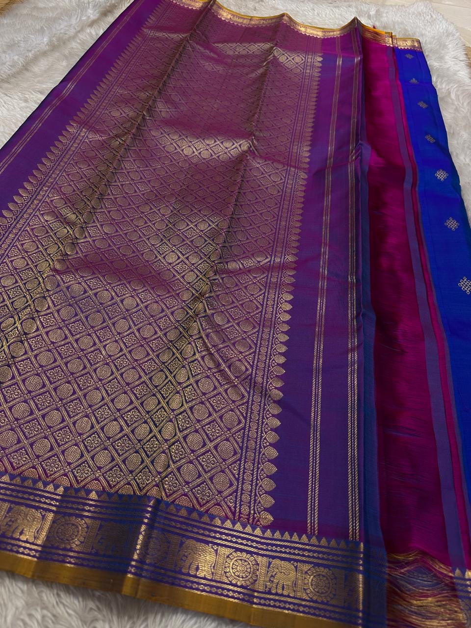 Sapphire Orchid celebrates the classic blue–purple pairing of Kanchi. The body is a rich sapphire/cobalt blue with tiny floral buttas in gold zari. A striking amethyst-purple korvai border and grid pavun Zari pallu Silk Mark Certified, delivery in 2 weeks