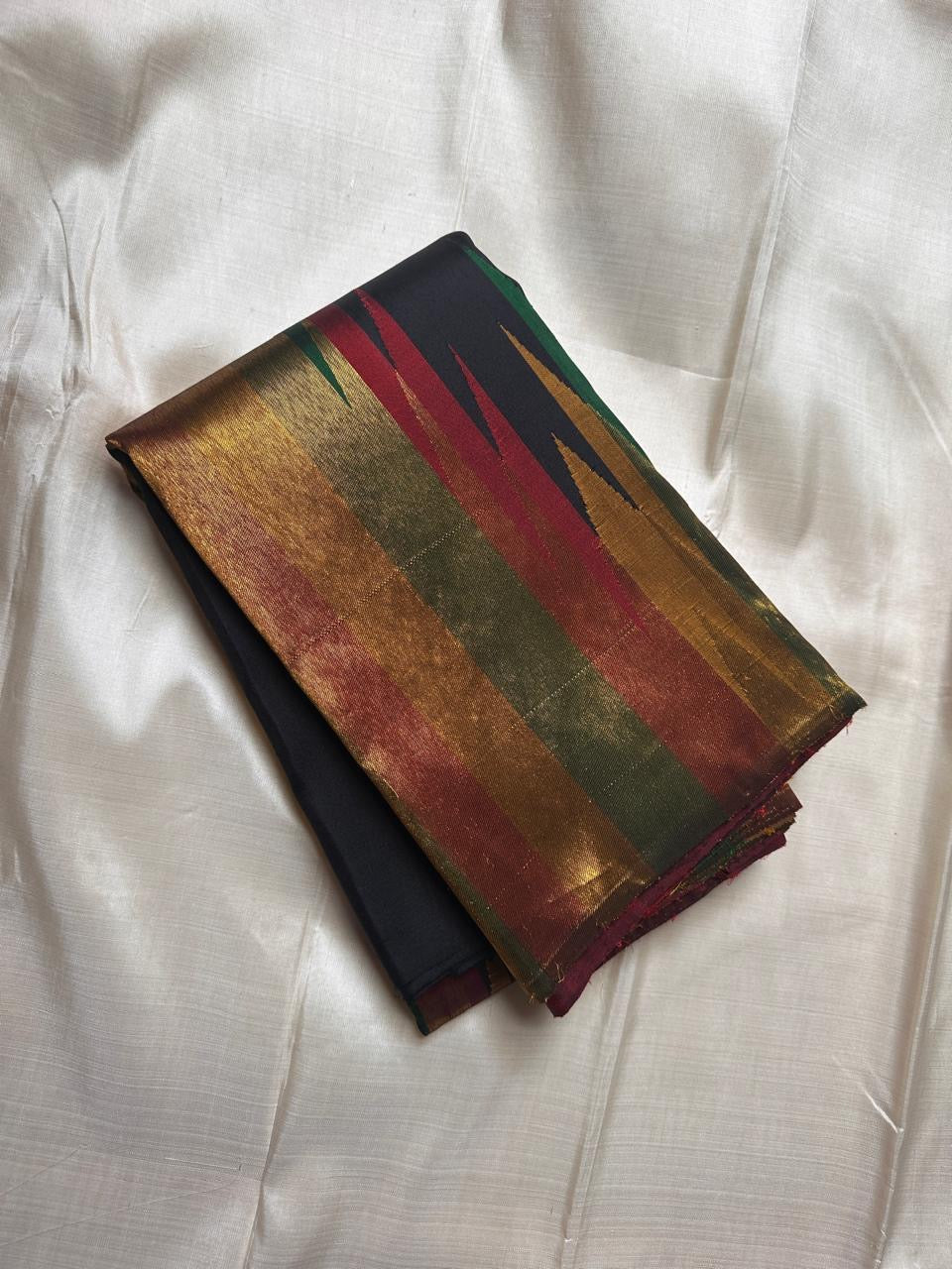 Black Kanchipuram silk saree folded with gold, green, and red Ettukol flame motif