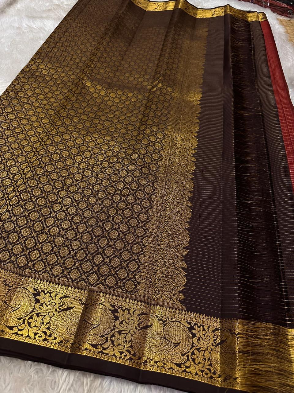 Mantra – Ruby Red coffee brown Kanchipuram Silk Saree with zari Checks with small buttas all over and Antique Peacock zari Border  showcasing regal peacocks and floral vines. A richly detailed pallu completes this heritage Zari kattam
