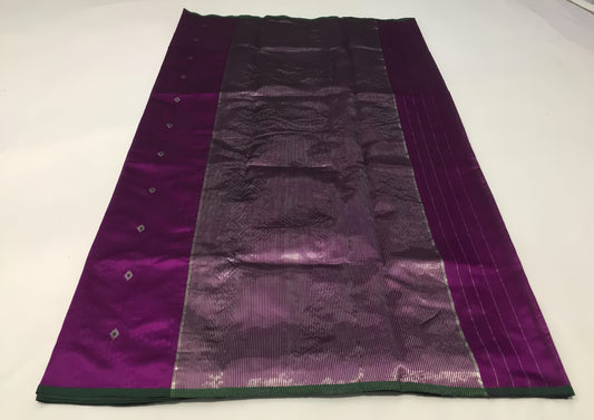 Draped in deep violet and plum, this pure silk Chanderi saree glows with a gentle sheen and graceful vertical zari lines. Delicate diamond meenakari motifs and finely woven borders lend a touch of tradition, with a  contrast green selvedge