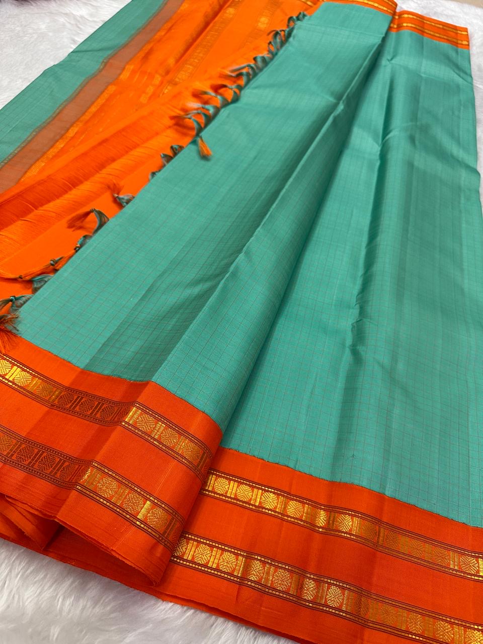 Sharvani blue sea green – sea green  Checked Silk Saree with an Orange red  shot color Zari Border & Vibrant Pallu A timeless silk saree featuring a cream body with delicate red checks, complemented by a striking churan orange  zari border pallu.