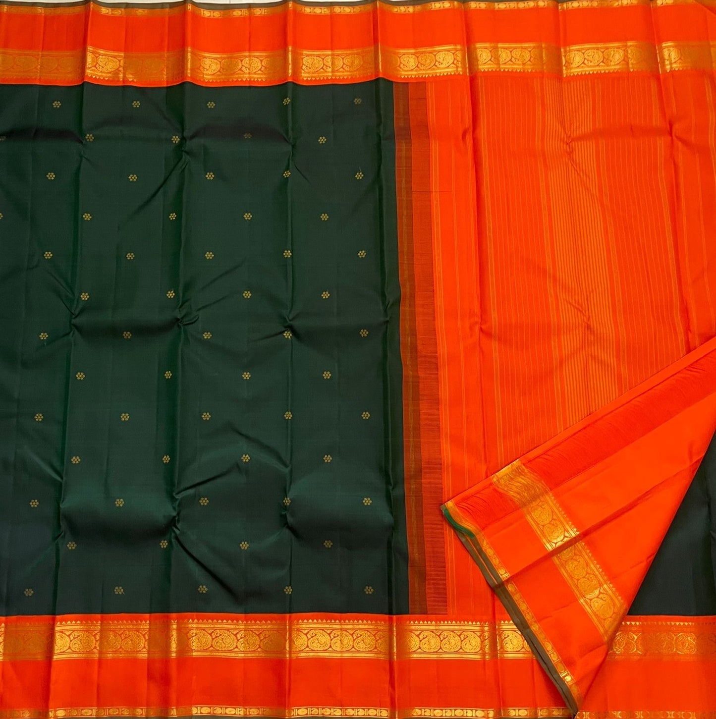Pachai Kesar Mayil — Kanchipuram Pure Silk

 Bottle-green body with dainty gold floral buttas

Contrast marigold-orange korvai borders with temple edging

Rich gold-zari paisley scrolls; striped orange pallu with tassels

Silk Mark Certified | Free Shipp