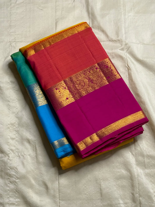 Varna Jaalam — Kanchipuram Pure Silk

Manjal yellow body with gold chakram buttas

Rani pink korvai border with floral & coin zari panels

Magenta–orange chevron pallu with blue–green color block top

Silk Mark Certified • Free Shipping within USA •