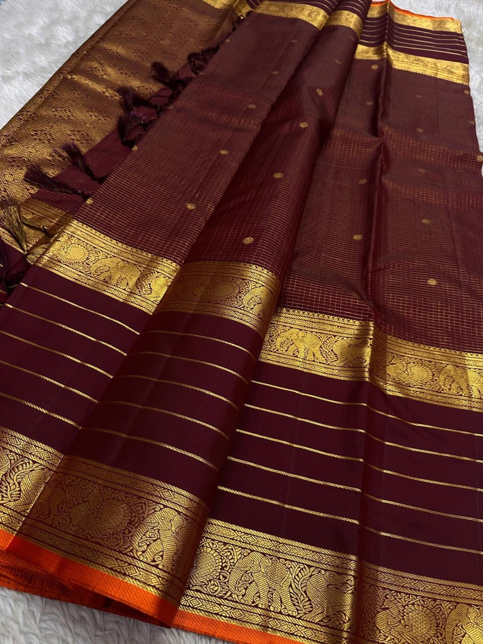 Open view of maroon Kanchipuram silk saree with tasselled pallu, horizontal zari lines and intricate gold yali–elephant borders.