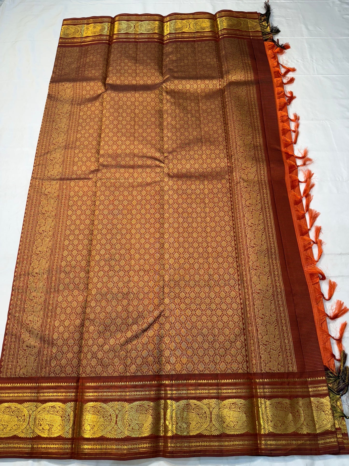 TEJAS – Vibrant Rust Orange Podi Kattam Kanchipuram Silk Saree

Micro-checks body with scattered gold chakram buttas; rich contrast maroon korvai borders

Grand circular annapakshi medallions in lustrous zari; ornate-jaal pallu & tassels

Silk Mark