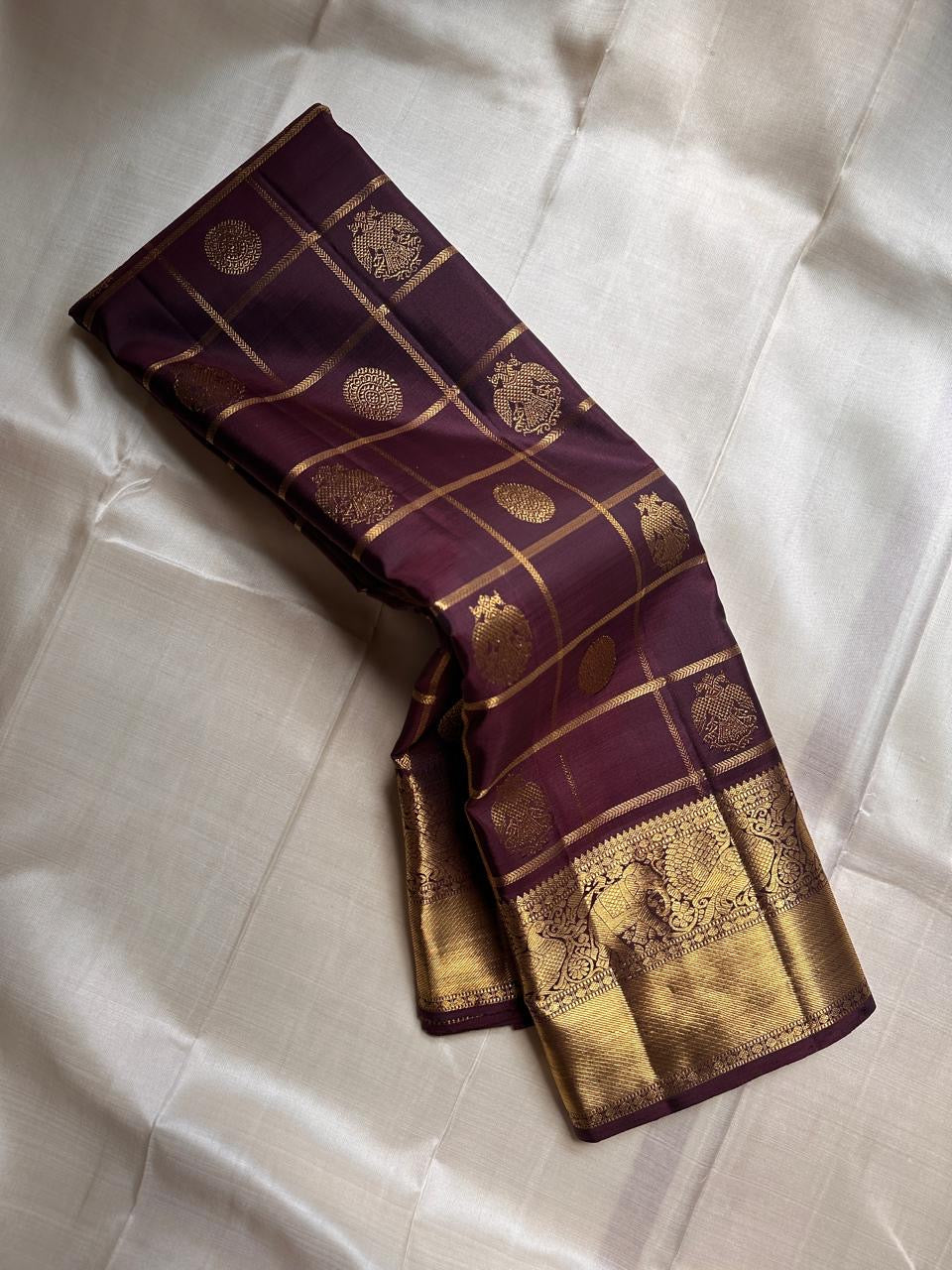 Folded view of plum Gandaberunda zari kattam Kanchipuram silk saree with rich gold elephant border on ivory base.