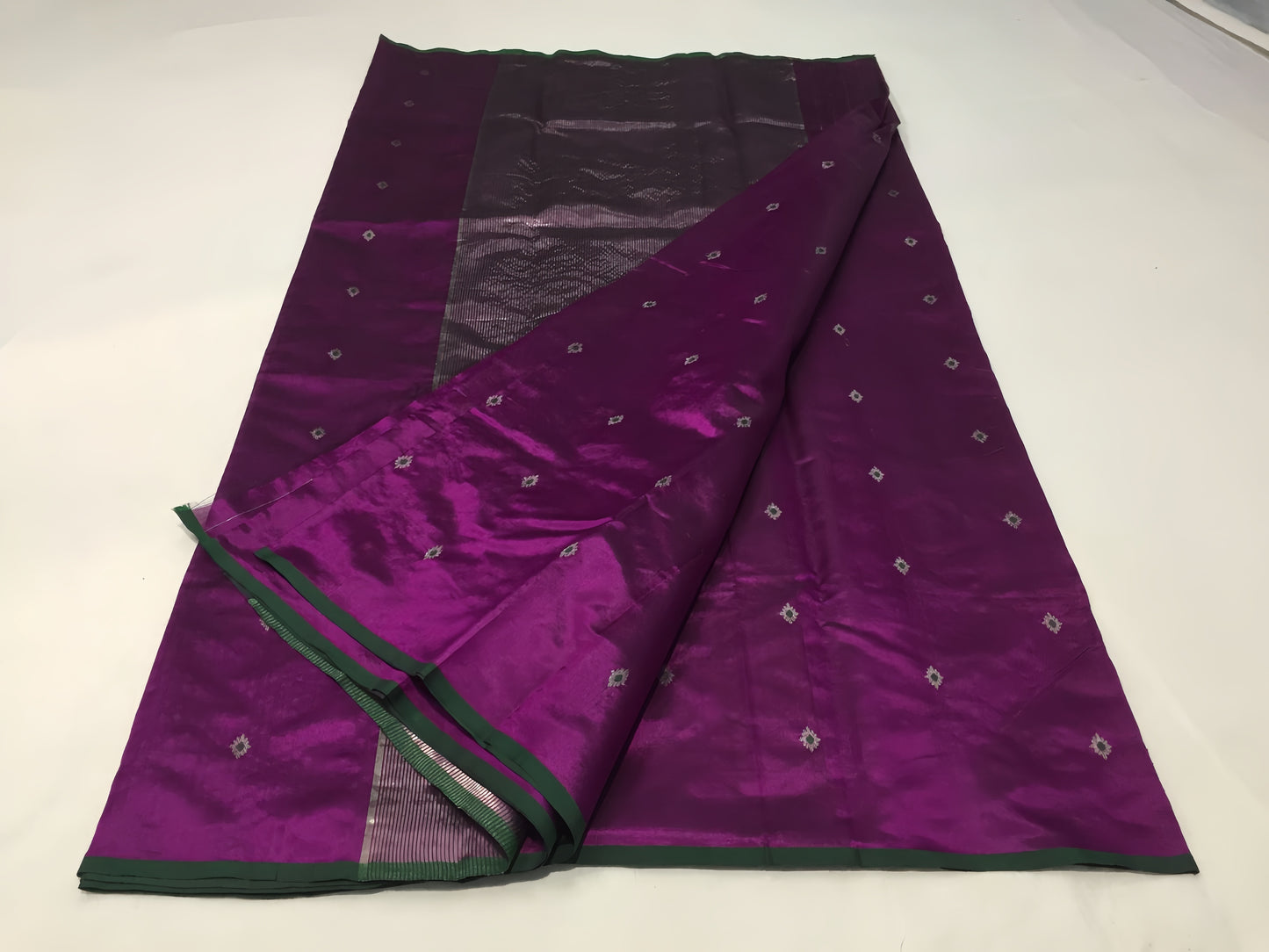 Draped in deep violet and plum, this pure silk Chanderi saree glows with a gentle sheen and graceful vertical zari lines. Delicate diamond meenakari motifs and finely woven borders lend a touch of tradition, with a  contrast green selvedge