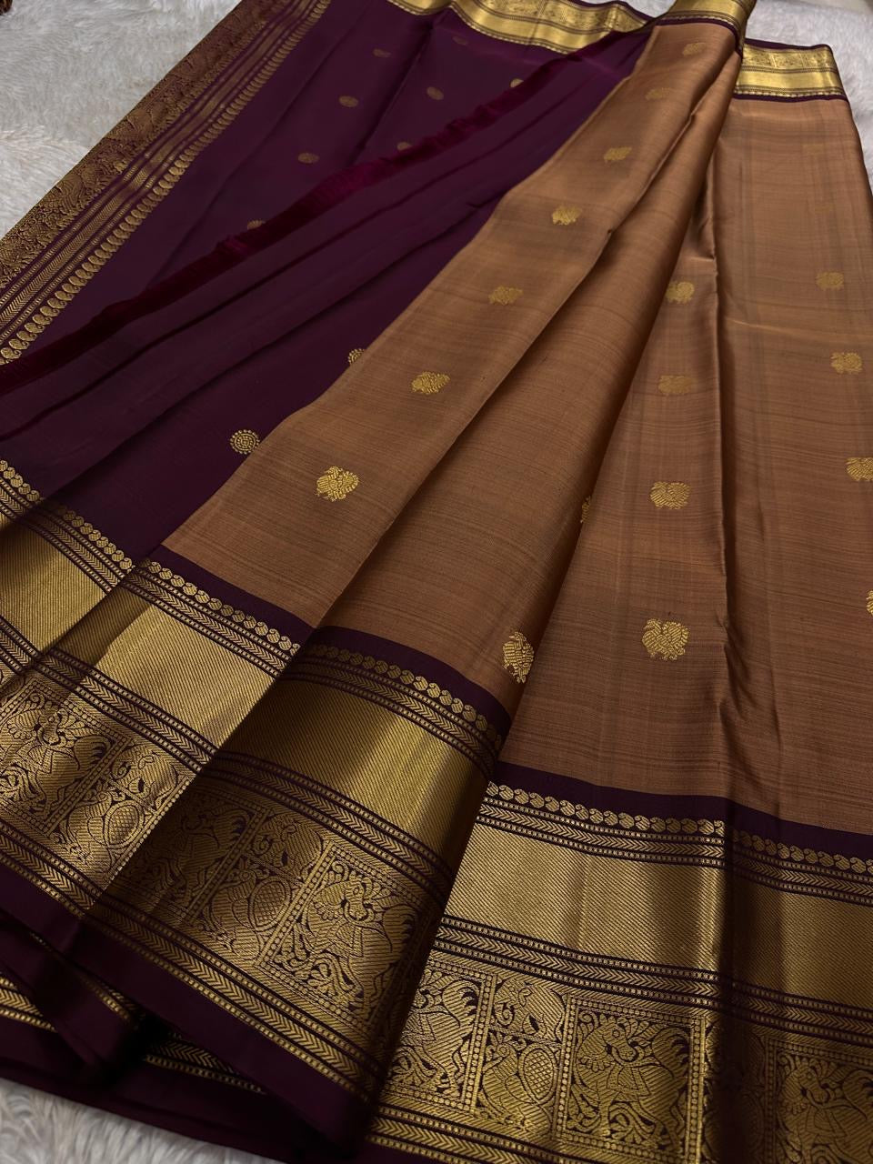 Pari is a graceful Kanchipuram pure silk saree in a serene copper-rose gold brown hue. Scattered peacock zari buttas .  Framed by an antique-gold korvai border temple-inspired yali, annam, and floral medallions, finished with a deep wine-maroon Pallu