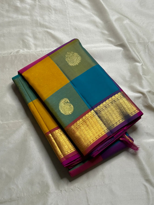 Rangoli Kattam – Pure Silk Kanchipuram Saree
Vibrant multicolor kattam checks with golden zari buttas across the body
Rich rani pink pallu with intricate zari weaving for a grand finish
Contrast purple borders edged with gleaming zari motifs