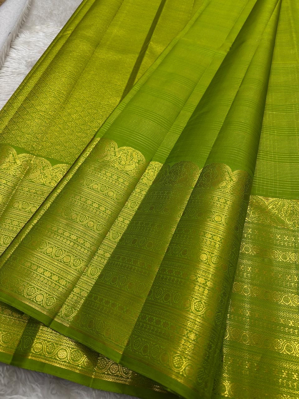 A radiant parrot green Kanchipuram silk saree that dazzles. The body features a delicate grid-like zari weave with small gold buttas scattered. The rich gold zari pallu stands out with grand temple-inspired arches and intricate motifs.