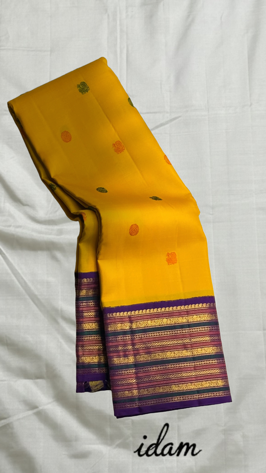 Swarna Kanakam Mayil Chakram — Pure Kanchipuram Silk Saree
Radiant turmeric-gold body adorned with silk-thread mayil and chakram buttas, framed by a regal vadamalli zari-woven korvai border and rich purple pallu.
Silk Mark Certified • Blouse Stitching Ava