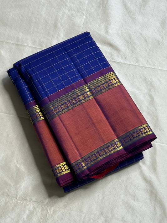 Indra Neelam Kattam – Pure Kanchipuram Silk Saree
Royal Blue Body with Fine Zari Grid Checks
Copper-Rose Korvai Borders with Floral & Chevron Zari
Grand Purple Pallu with Tassels
Silk Mark Certified | ships in 2  weeks | Blouse Stitching Available