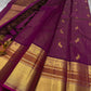 Full view of magenta Kanchipuram silk saree with peacock buttas and grand gold zari borders laid out on a surface